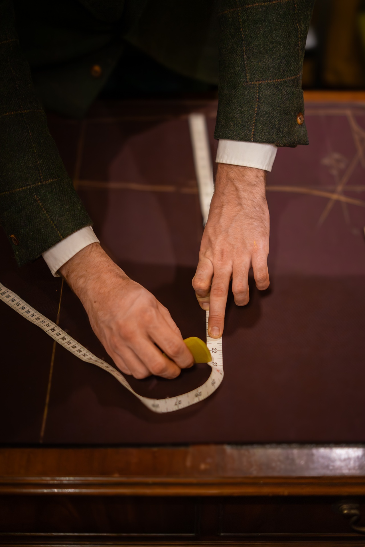 Hands taking a measurement with a tape on a leather-topped cutting table